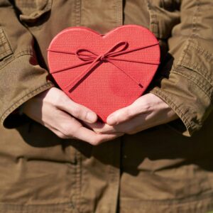 Someone in a brown coat holding a red heart box in front of them